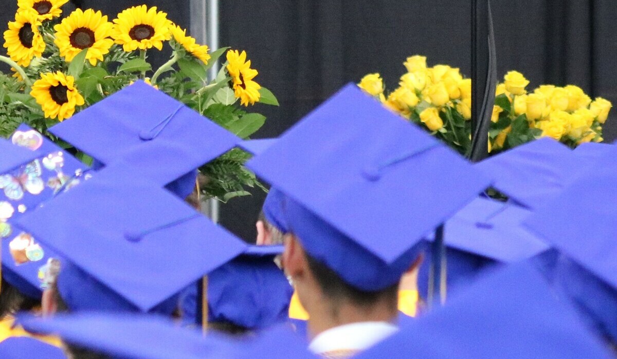 close up of hats of grads sitting during ceremonies with flowers in the background